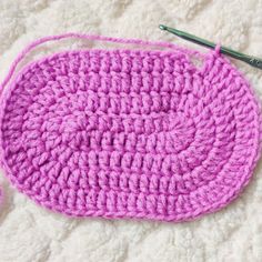 a crocheted pink oval dishcloth on a white surface next to a knitting needle