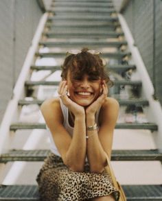 a woman sitting on the steps smiling and holding her hand to her face with both hands