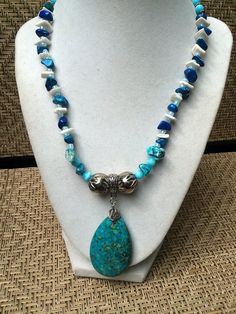 "This vibrant gemstone and sea shell necklace set is handmadeartfully arranging turquoise Howlite gemstones with blue rock quartz, blue glass beads, pieces of white seashell, silver Rhodium accent beads and small silvertone metal beads.  It is further enhanced with a turquoise stone  pendant which measures an inch and a half (4cm) wide and 2\" (5cm) long.   The necklace measures 18\" (46cm)  long excluding the pendant, and is finished with a decorative silver ring clasp. The matching bracelet st Blue Turquoise Teardrop Necklace With Gemstone Beads, Blue Teardrop Turquoise Necklace With Natural Stones, Blue Gemstone Jewelry For The Beach, Bohemian Howlite Jewelry With Natural Stones, Southwestern Turquoise Jewelry For Beach, Artisan Turquoise Necklace With Natural Stones For Beach, Blue Turquoise Necklace With Stones, Unique Blue Turquoise Necklace With Stones, Blue Howlite Beaded Necklaces As Gift