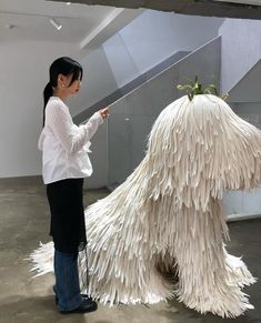 a woman standing next to a giant white dog made out of fake feathers and grass