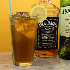 a bottle of jack daniels next to a glass filled with ice and lemon wedges