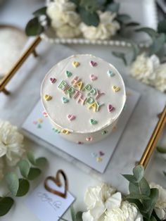 a birthday cake sitting on top of a table next to white flowers and greenery