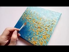 someone is painting on a blue and yellow piece of paper with gold flecks