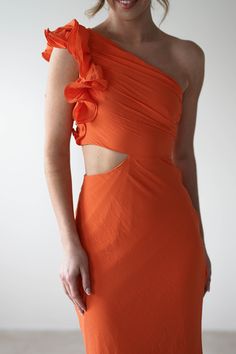 a woman wearing an orange dress with one shoulder cut out and flowers on the side