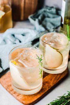 two glasses filled with ice sitting on top of a wooden cutting board