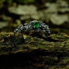 a green ring sitting on top of a mossy rock next to some leaves and rocks