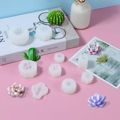 a pink table topped with white candles and small cactus plants next to a box of fake flowers