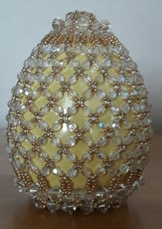 a yellow beaded vase sitting on top of a wooden table next to a wall