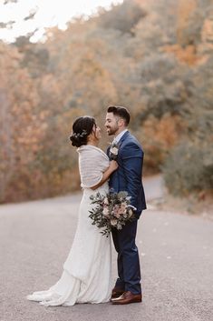 a bride and groom standing on the side of a road in front of some trees