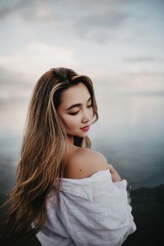 a woman with long hair standing in front of the ocean and looking off into the distance