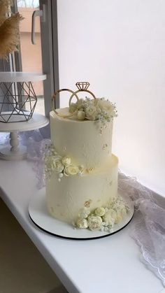 two tiered wedding cake sitting on top of a white table next to a window