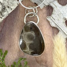 Petoskey Stone from Michigan, handcrafted into a cabochon and set in a custom, Sterling Silver bezel setting. Includes an 18 inch, solid sterling silver 1.1mm snake chain with clasp. The stone measures approximately 0.9 x 1.1 inches.  Overall pendant height is approximately 1.5 inches. The name Petoskey appears to have originated late in the 18th century.  Its roots stem from an Ottawa Native American legend. In 1965, the Petoskey Stone became the state stone of Michigan. Petoskey stone helps us Untreated Sterling Silver Round Pendant, Artisan Oval Jewelry With Bezel Setting, Untreated Sterling Silver Necklaces In Silver, Sterling Silver Cabochon Necklace For Anniversary, Sterling Silver Jewelry With Bezel Setting In Round Pendant, Silver Sterling Silver Necklace, Oval Sterling Silver Necklace With Lobster Clasp, Untreated Sterling Silver Necklaces As Gifts, Sterling Silver Pendant With Bezel Setting