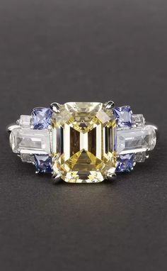 a fancy yellow diamond ring with blue and white stones on the sides, set in 18k white gold