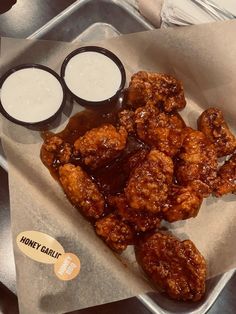 a tray with some chicken wings and two cups of sauce on it next to a spoon