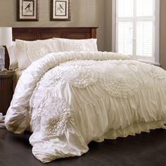 a white comforter with ruffles on it and two framed pictures above the bed