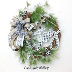 a christmas wreath with the word joy on it and pine cones, evergreen leaves, and plaid ribbon