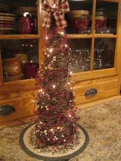 a small christmas tree with lights on it in front of a shelf filled with dishes