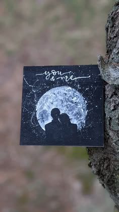 a piece of paper that has been placed on top of a tree with an image of two people under the moon