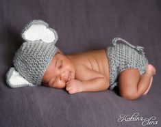 a newborn baby wearing a crochet hat and diaper is laying on a gray blanket