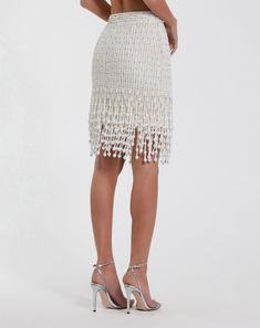 the back view of a woman wearing a white skirt with fringe trims and heels