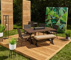 a table and chairs are on a wooden platform in the grass near a painting with green leaves