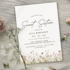 a white wedding card with flowers and greenery next to it on top of a table