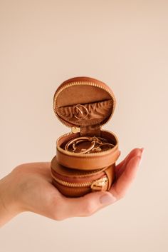 a hand holding an open leather jewelry box with two rings in it's lid