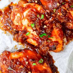 chicken wings covered in bbq sauce and garnished with scallions on parchment paper