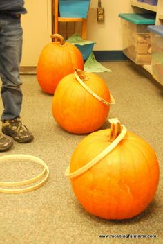 three orange pumpkins sitting on the floor in front of a person standing next to them