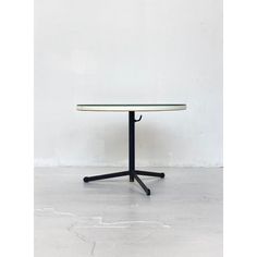 a white table with black legs and a round glass top on an empty room floor