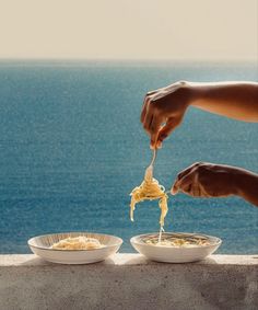 two people are eating noodles off the edge of a cliff overlooking the ocean and blue water