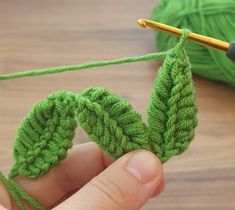 someone is crocheting the leaves on a green yarn skeing with a knitting needle