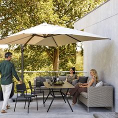 two women and a man are sitting under an umbrella on a patio with tables and chairs