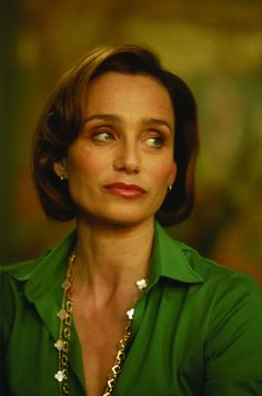 a woman wearing a green shirt and gold necklace looking at the camera with an intense look on her face