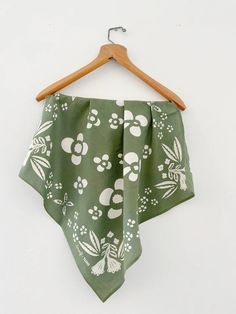 a green bandana with white flowers and leaves on it hanging from a wooden hanger