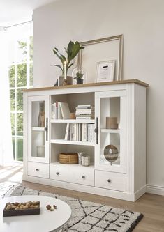 a living room with a white bookcase and some plants on top of the bookshelves