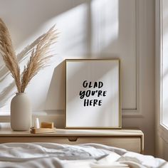 a white vase sitting on top of a wooden dresser next to a framed poster that says glad you're here