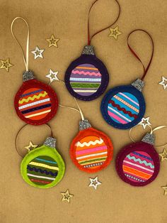 four ornaments are hanging on a brown surface with stars around them and one is decorated in multi - colored stripes