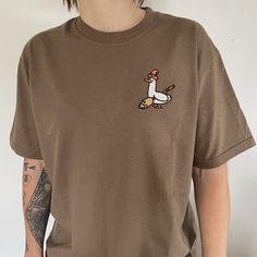 Brown organic t shirt with an embrodiered silly goose  Witchy Silly Goose T- Shirt with Halloween theme embroidery design. 👻 Unisex relaxed fit  ✨Classic silly goose dressed and ready for Haloween! Witchy goose✨ If you would like a size or colour that you can't see here then please don't hesitate to message us as we would love to try to accommodate your request as best we can 😊  ✨By buying a little something from us you will supporting a small business (entirely ran by just 2 lovely ladies ️)! Fall T-shirt With Embroidered Text And Relaxed Fit, Custom Embroidery Relaxed Fit T-shirt For Fall, Embroidered Relaxed Fit T-shirt For Fall, Fall Embroidered Graphics Short Sleeve T-shirt, Fall Embroidered Short Sleeve T-shirt, Embroidered Short Sleeve T-shirt For Fall, Casual Embroidered Halloween T-shirt, Custom Embroidery Short Sleeve T-shirt, Goose Dress