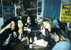 four people sitting at a table drinking beer and posing for the camera with posters on the wall behind them