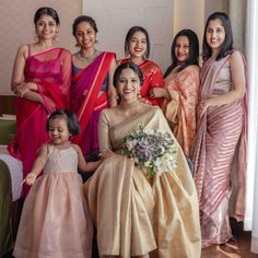 a group of women standing next to each other in sari dresses and holding bouquets