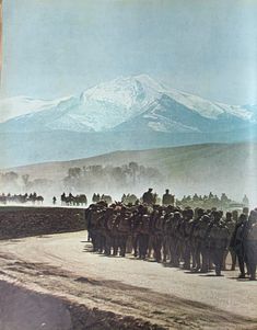 a group of men standing on the side of a dirt road next to a mountain