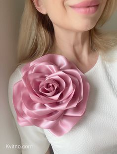 a woman wearing a white shirt and pink flower brooch on her neck with long blonde hair