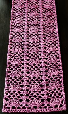 a pink crocheted table runner sitting on top of a wooden table