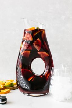 there is a vase with fruit in it next to two glasses and an ice cube