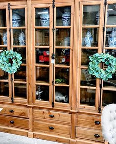 a wooden china cabinet with glass doors and two wreaths on top