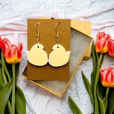 a pair of bird earrings sitting on top of a card next to tulips