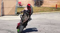 a man riding on the back of a motorcycle down a street next to a fence