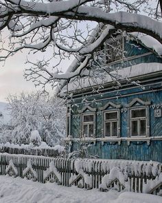 a blue house covered in snow next to a fence and tree with no leaves on it