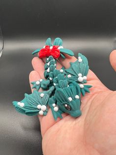 a hand holding a small green and red brooch with white beads on it's fingers